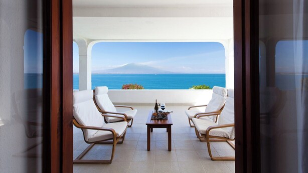 A balcony with white chairs and a table, overlooking a clear blue sea and a distant mountain. - Villa Saracena - Seven Bedroom Villa, Sleeps 14 (Costa Saracena - Castelluccio)