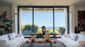 Un salon moderne avec des canapés blancs, une table basse en bois et une grande fenêtre donnant sur un paysage magnifique.