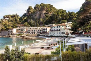 A coastal hotel with multiple buildings, a beach with sun loungers, and a rocky cliff in the background. - Ortensia - Four Bedroom Villa, Sleeps 8 (Mascali)