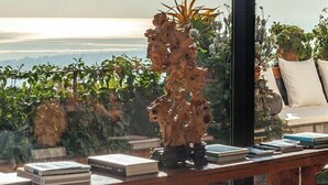 Une pièce baignée de lumière naturelle, avec vue sur la mer, comprenant une table en bois ornée de livres et d’une plante décorative.