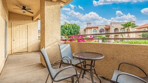 A balcony with a table and chairs, a ceiling fan, and a view of a building with a red roof. - Sunlit Oasis Condo w/ Pool & Patio / First Floor (Phoenix)