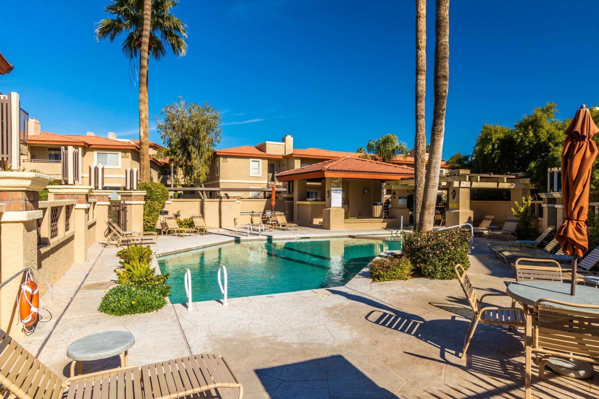 A pool area with lounge chairs and umbrellas, surrounded by buildings with red-tiled roofs.