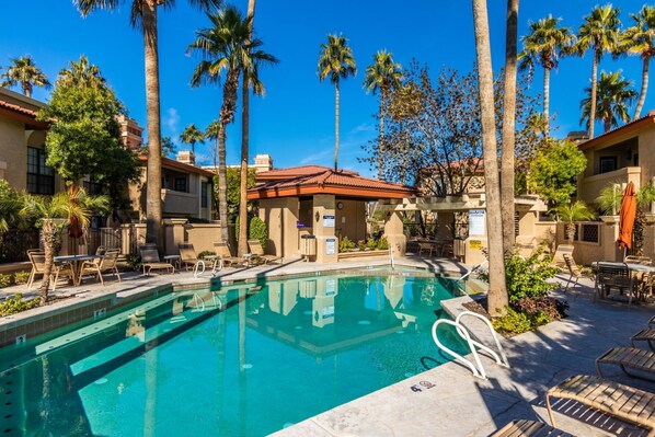 A swimming pool surrounded by palm trees and lounge chairs, with a building in the background. - Sunlit Oasis Condo w/ Pool & Patio / First Floor (Phoenix)