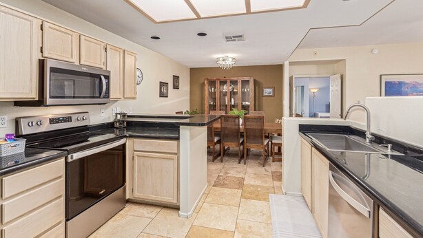 A modern kitchen with a central island, built-in microwave, stainless steel appliances, and a dining area with a chandelier. - Sunlit Oasis Condo w/ Pool & Patio / First Floor (Phoenix)