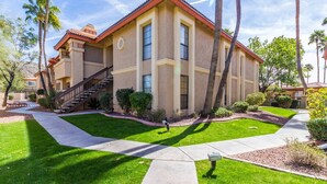 A two-story building with a red-tiled roof, a central staircase, and a well-maintained lawn with palm trees. - Sunlit Oasis Condo w/ Pool & Patio / First Floor (Phoenix)