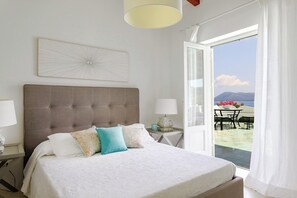 A bedroom with a large bed, a view of the outdoors, and a table with flowers.