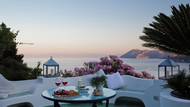 A terrace with a table set for two, overlooking a body of water and mountains. - Posidonia - Seven Bedroom Villa, Sleeps 14 (Lipari)