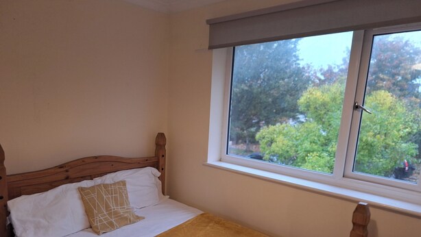 Una cama bien hecha con cabecera de madera, una ventana con vistas a árboles y una toalla sobre la cama.