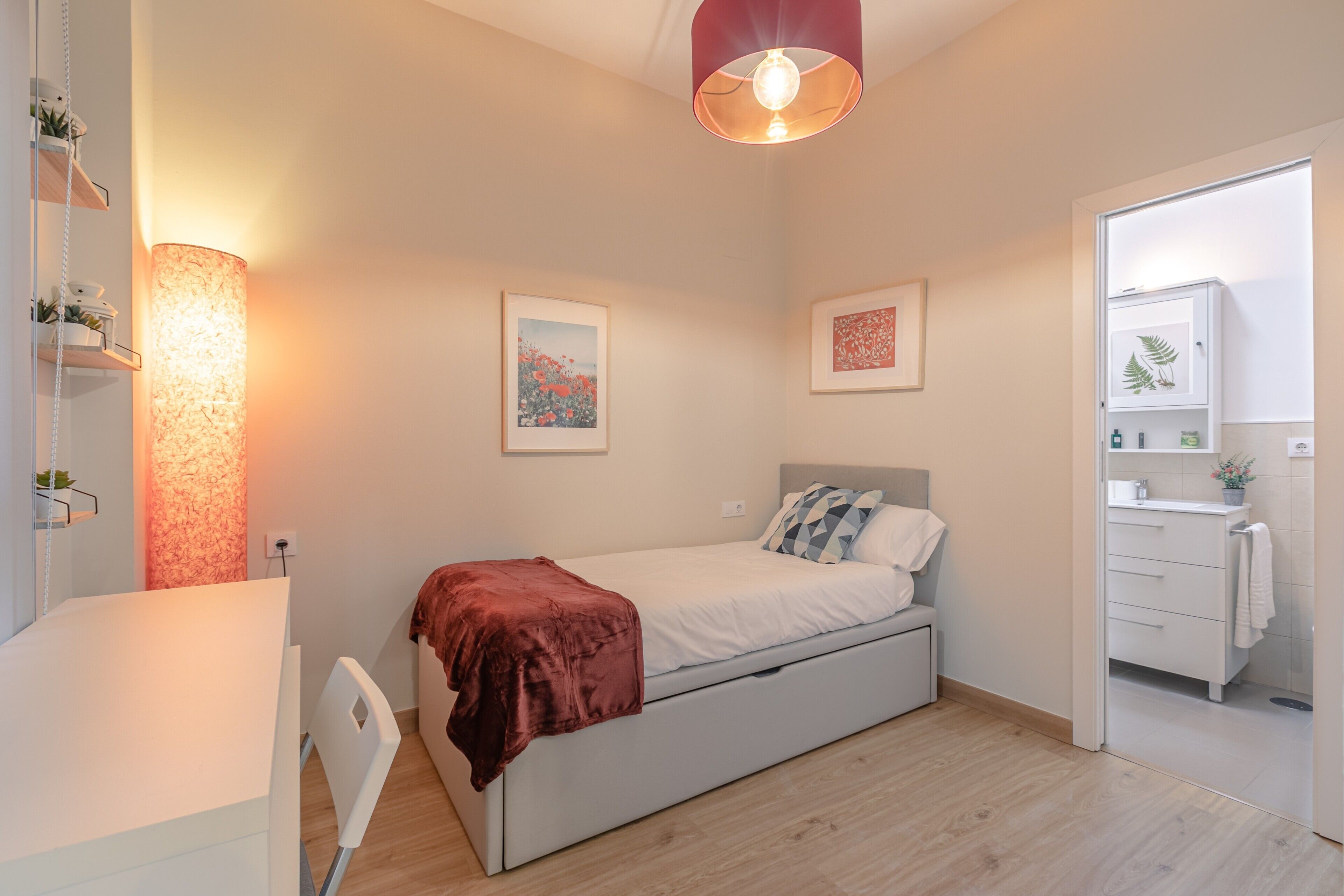 A bedroom with a bed, bedside table, lamp, and artwork on the wall.