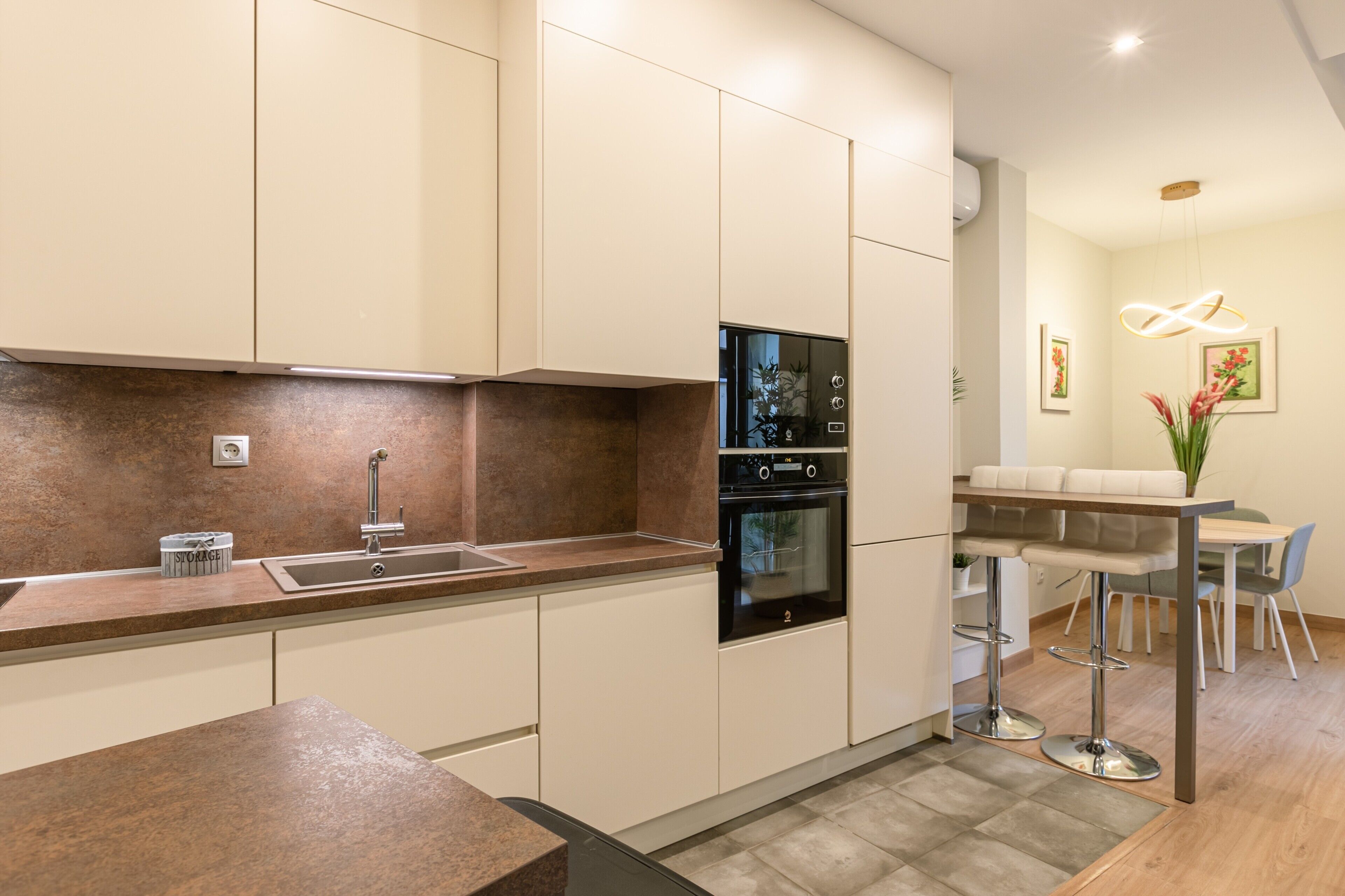 Een moderne keuken met een ingebouwde oven, een spoelbak en een eethoek met een tafel en stoelen.