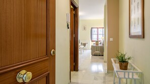 Un pasillo con una puerta de madera, un banco blanco con una planta y un cuadro en la pared.