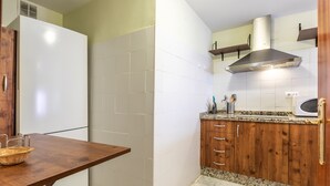 Cocina compacta con refrigerador blanco, armarios de madera, encimera de granito y extractor de acero inoxidable.