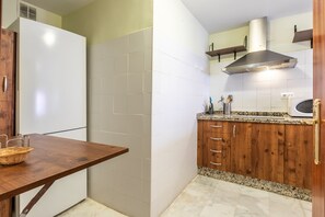 Eine kompakte Küche mit einem weißen Kühlschrank, Holzschränken, einer Arbeitsplatte aus Granit und einer Edelstahl-Dunstabzugshaube.