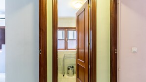 Un pasillo que lleva a un baño con ventana, un perchero y un cubo de basura.