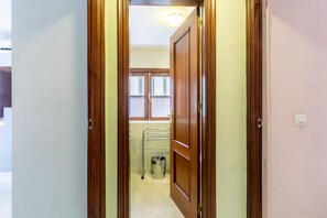 Ein Flur, der zu einem Badezimmer mit Fenster, Handtuchhalter und Mülleimer führt.