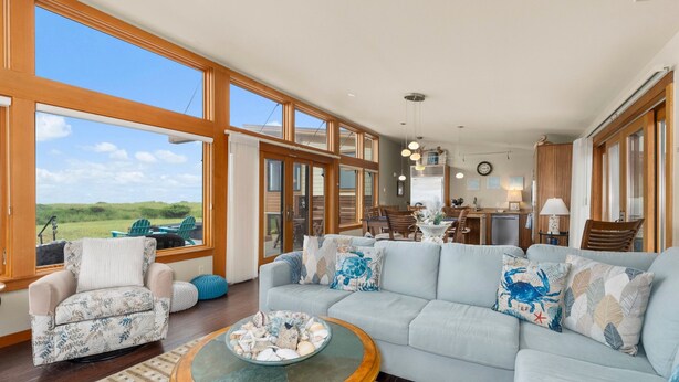 A spacious living room with a large light blue sofa, a round coffee table, and a view of the outdoors through large windows. - Oceanfront Escape in Westport, WA (Westport)