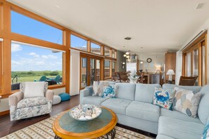 A spacious living room with a large light blue sofa, a round coffee table, and a view of the outdoors through large windows. - Oceanfront Escape in Westport, WA (Westport)