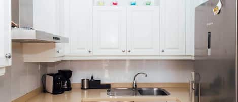 Een moderne keuken met witte kasten, een Bosch koelkast, een spoelbak en een koffiezetapparaat.