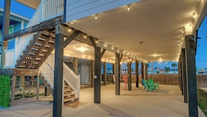 A covered outdoor area with a wooden staircase, string lights, and green chairs. - Bright Coastal Escape w/ Games, Swing Chairs & Minutes to Port A Beach Captain Kirk by Avantstay (Port Aransas)