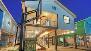 A two-story building with a basketball hoop, a staircase, and a covered porch area. - Bright Coastal Escape w/ Games, Swing Chairs & Minutes to Port A Beach Captain Kirk by Avantstay (Port Aransas)