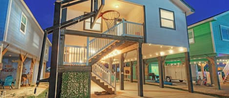 Un edificio de dos pisos con un aro de baloncesto, una escalera y un porche cubierto.