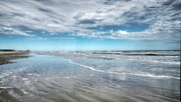 A beach with waves, a clear sky, and distant buildings. - Bright Coastal Escape w/ Games, Swing Chairs & Minutes to Port A Beach Captain Kirk by Avantstay (Port Aransas)