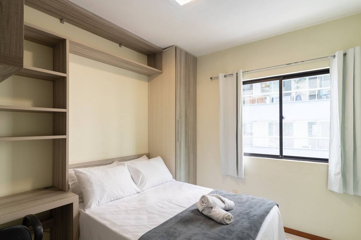 A bedroom with a bed, a desk, and a window.