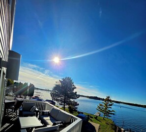 Een balkon met tuinmeubilair met uitzicht op een meer, heldere lucht en een stralende zon.