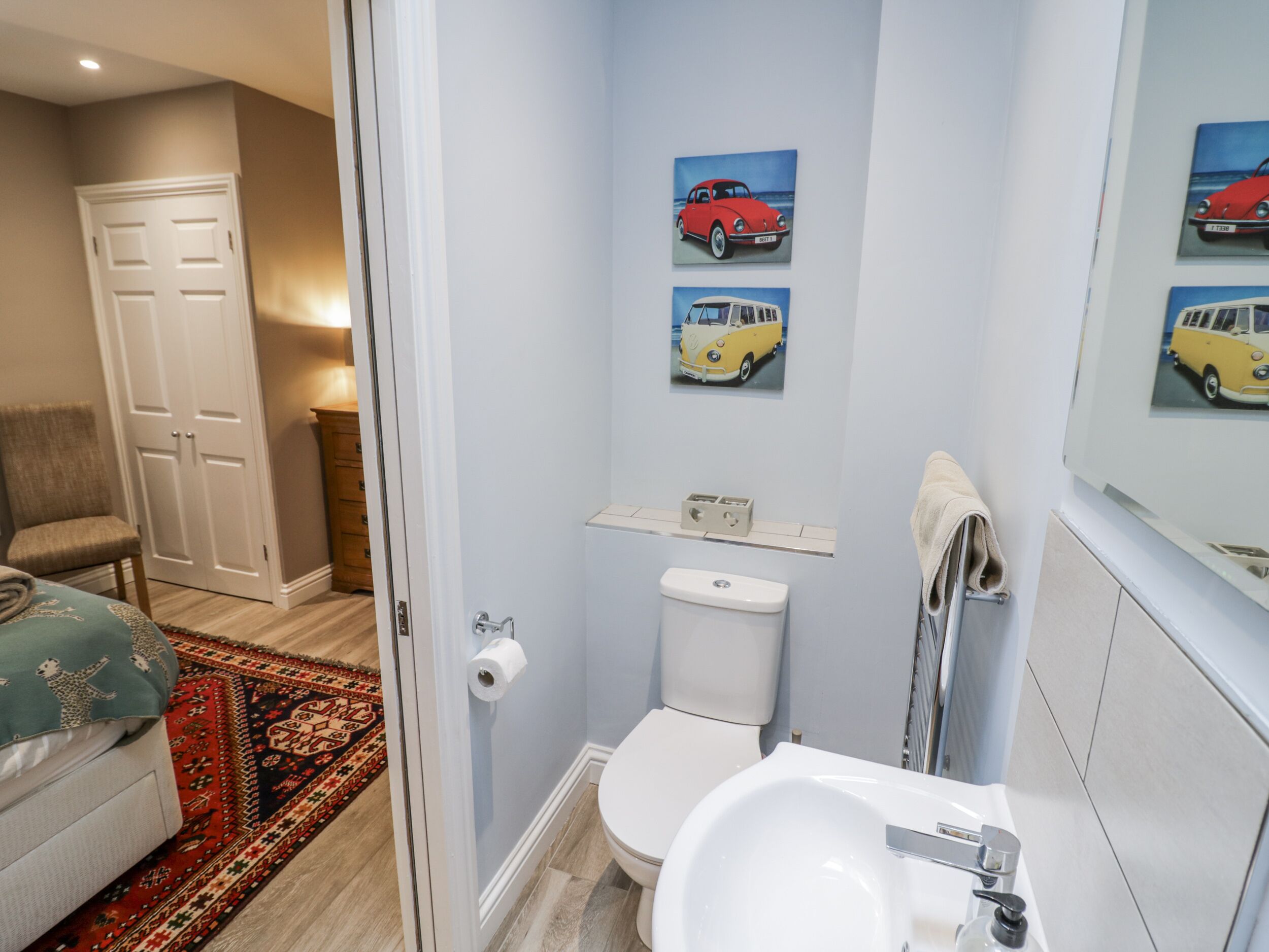 A bathroom with a toilet, sink, and a mirror. There are wall-mounted pictures of vintage cars.