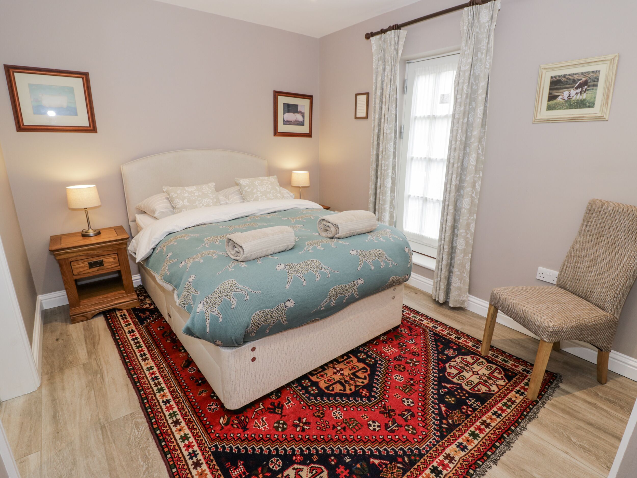 A bedroom with a bed, bedside tables, a chair, a window with curtains, and a rug.