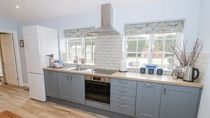 A modern kitchen with grey cabinets, a built-in oven, a stainless steel sink, and a window with a view of the outdoors. - Rose Stables (Bampton)