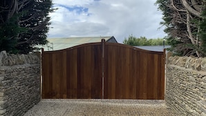 A wooden gate with a stone wall on either side, leading to a gravel driveway. - Rose Stables (Bampton)