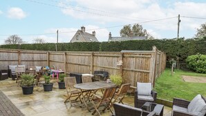 An outdoor patio with a wooden table and chairs, surrounded by potted plants and a wooden fence. - Rose Stables (Bampton)