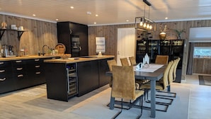 Una cocina moderna con una isla central, armarios oscuros y un comedor con mesa y sillas.