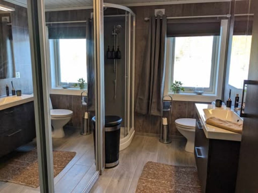 A modern bathroom with a glass shower enclosure, two toilets, and a sink area.