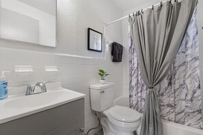 Ein Badezimmer mit einem weißen Waschbecken, einer Toilette und einem Duschvorhang mit Marmoroptik.