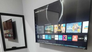 Un televisor de pared muestra varios servicios de transmisión y una cafetera con tazas sobre una mesa.