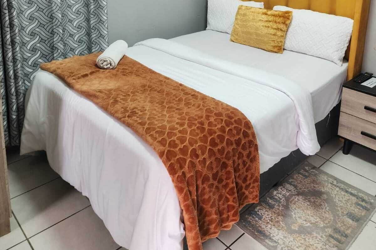 A bedroom with a bed, a nightstand, a towel, and a patterned curtain.