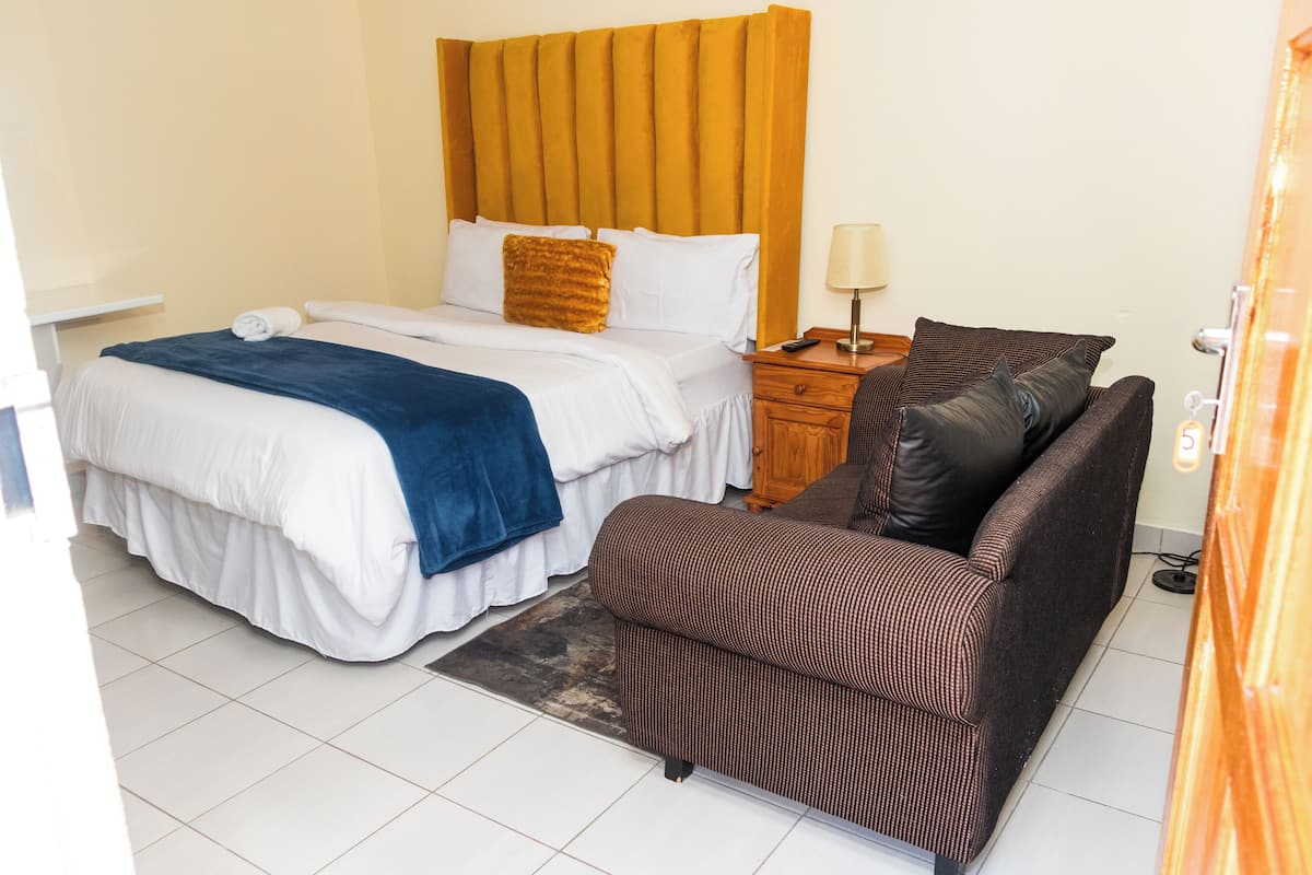 A hotel room with a bed, a sofa, a nightstand, and a lamp.