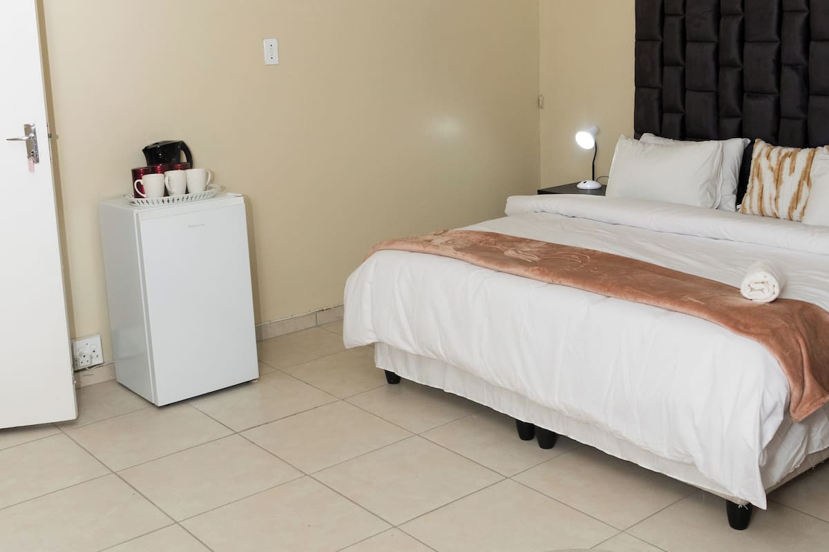 A hotel room with a bed, bedside table, and a small refrigerator.