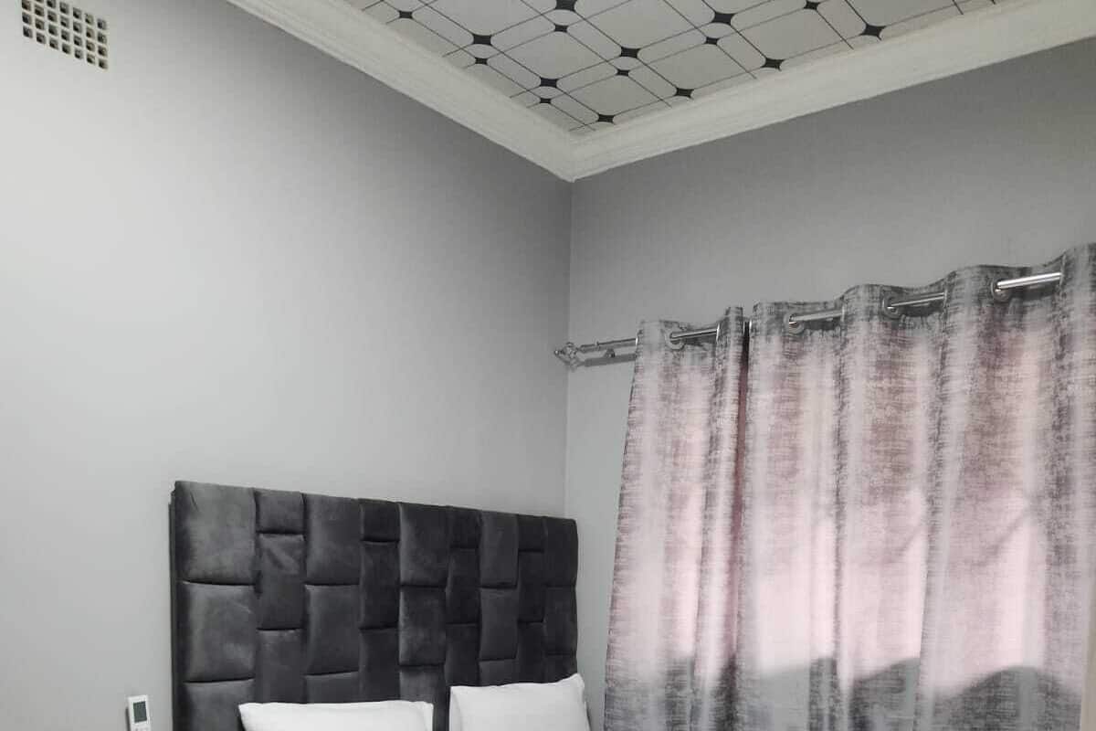 A bedroom with a bed, a bedside table, a chair, and a ceiling with a geometric pattern.