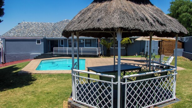 Un patio trasero con piscina, un pabellón con techo de paja y un área de patio con sillas y mesas.