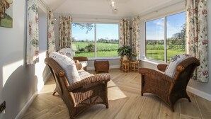 Una habitación amplia con muebles de mimbre, ventanas grandes y vistas a un campo verde.