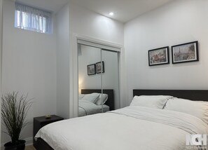 A bedroom with a bed, a nightstand, a potted plant, a wardrobe, and two framed pictures on the wall. - Modern 3-Bedroom Apartment in Luxury Home in Downtown Richmond Hill (Richmond Hill)