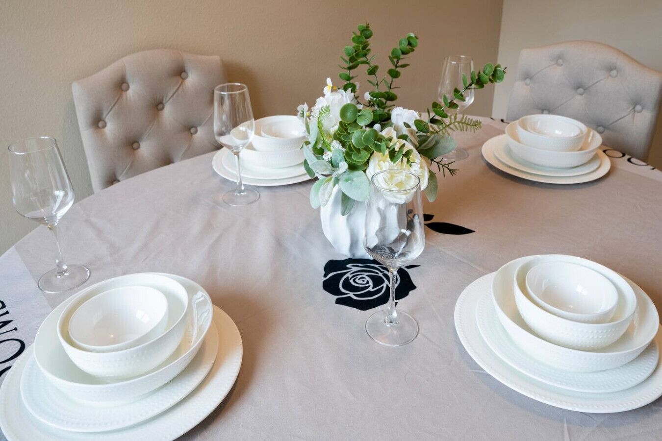 A round table set for a meal with white plates, bowls, and wine glasses.