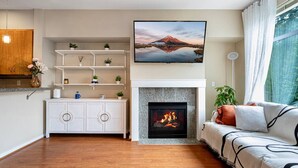 A living room with a fireplace, wooden flooring, a sofa, a TV, and a bookshelf.