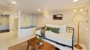 A bedroom with a bed, bedside table, lamp, and a view of a bathroom with a bathtub.