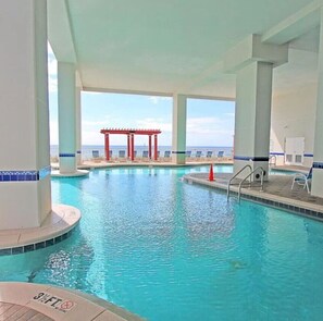 Ein großer, überdachter Pool mit klarem, blauem Wasser, umgeben von weißen Säulen und einer roten Pergola.