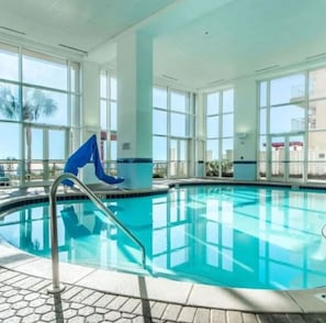 An indoor swimming pool with clear glass walls, a metal ladder, and a tiled floor. - Cozy Oceanfront Condo-Hot tubs-Pools (Panama City Beach)