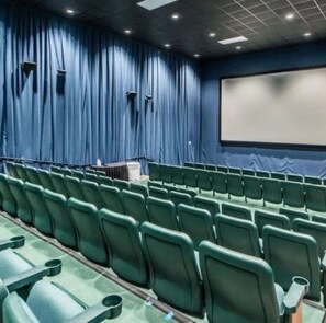 An auditorium with rows of green chairs, a stage with a podium, and a large screen. - Cozy Oceanfront Condo-Hot tubs-Pools (Panama City Beach)